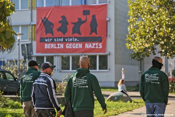 Großes Banner mit der Aufschrift "Wir sind viele. Berlin gegen Nazis" im Hintergrund eines Naziaufmarsches.