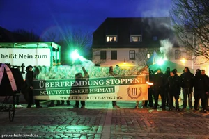 Personen posieren mit einem Banner der partei "Der III. Weg" und Pyrotechnik.