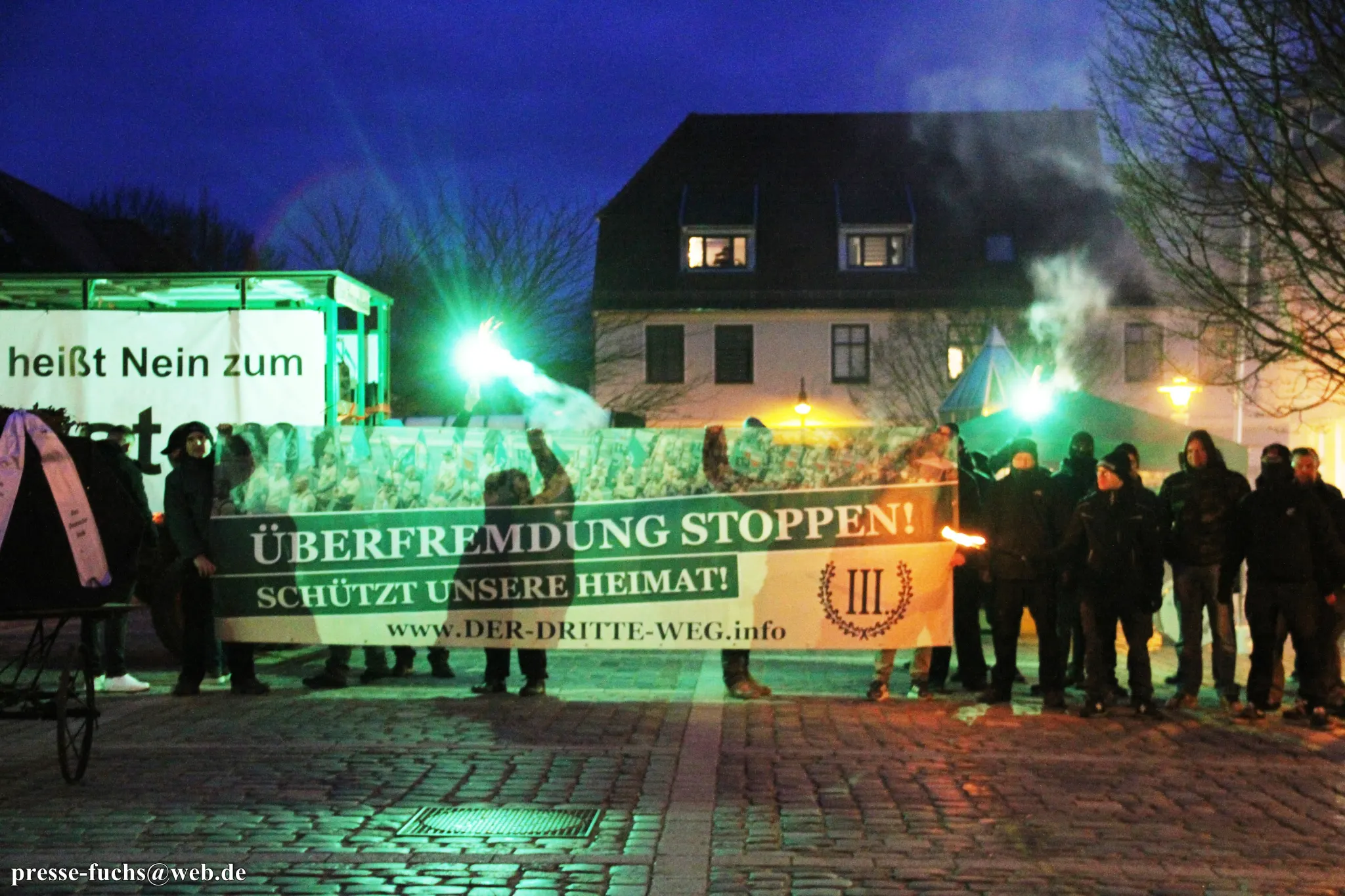 Personen posieren mit einem Banner der partei "Der III. Weg" und Pyrotechnik.
