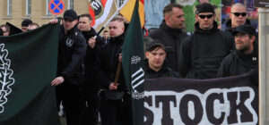 Schwarz gekleidete Personen hinter Bannern der Partei "der dritte Weg"
