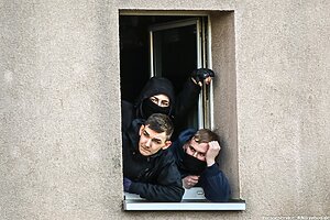 Drei vermummte bewaffnete Personen schauen aus dem Fenster