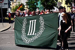 Personen tragen ein Transparent auf dem das Logo der Partei "der III. Weg" abgebildet ist.