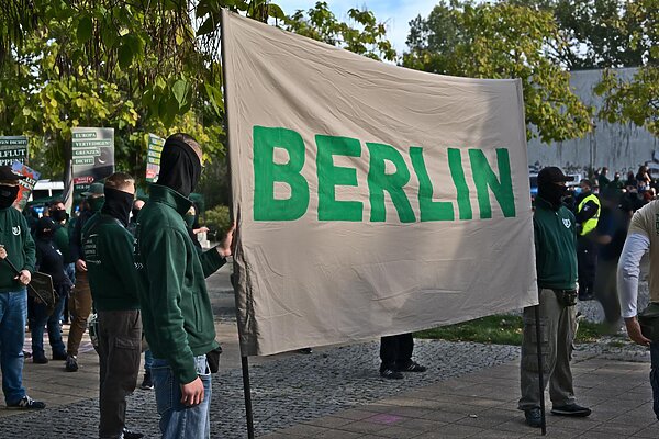 Zwei Vermummte Personen halten ein Banner mit der Aufschrift "BERLIN" auf einer rechten Demonstration.
