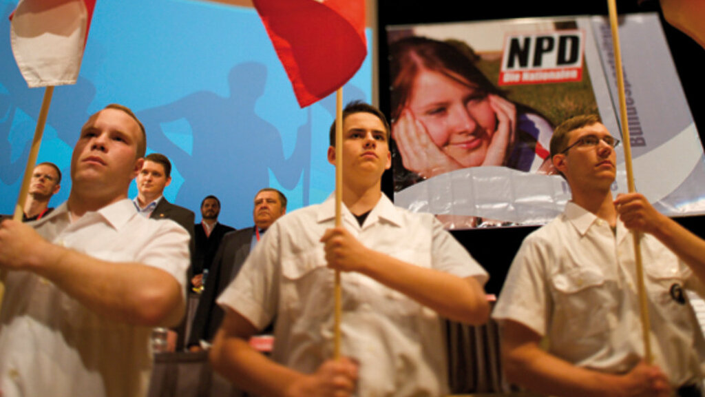Junge Personen in wei&szlig;en Hemden und NPD Fahnen in der Hand stehen in einer Reihe.