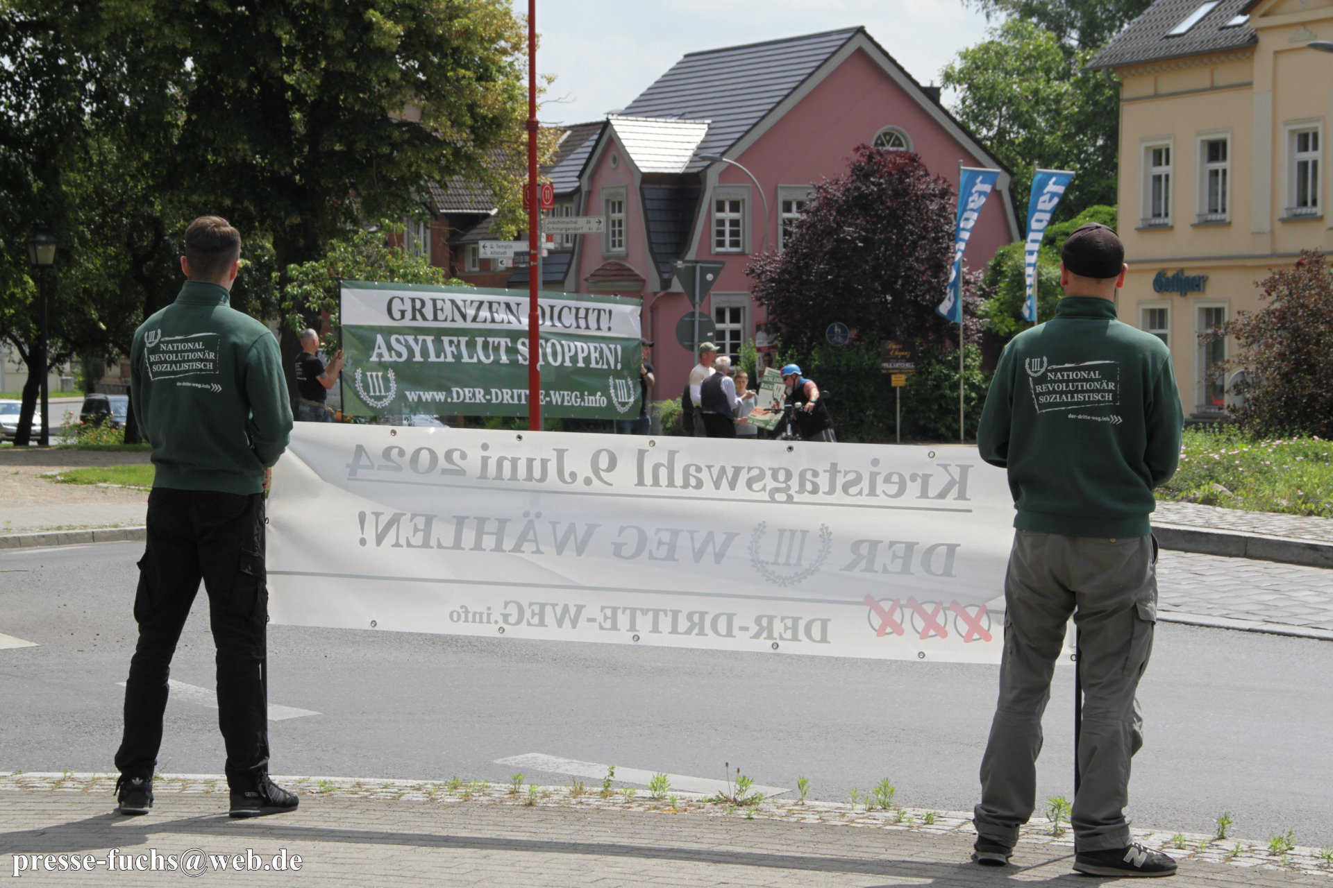 Personen an einer Straßenkreuzung. Sie tragen Banner und Kleidung der Partei "Der. III. Weg"