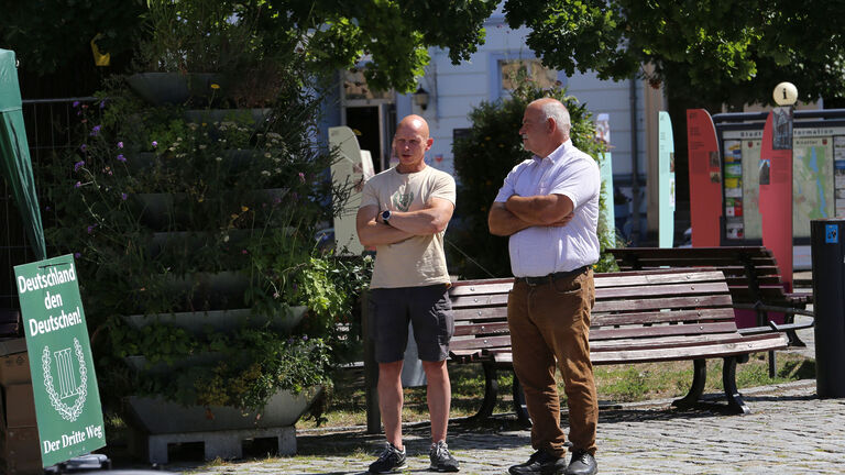 Zwei Personen stehen mit verschränkten Armen vor einer Parkbank